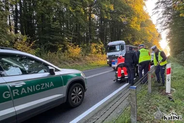 Straż graniczna i policja interweniują przy wypadku na leśnej drodze, gdzie ratownicy udzielają pomocy poszkodowanemu na noszach.